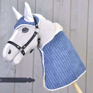 Set Manchester Plum od Hobby Horse LarDen obsahuje plyšového Hobby Horse s bílým obličejem, černou uzdečkou a modrým prošívaným přehozem plus ladící čabraku, naaranžované před světlou dřevěnou stěnou.