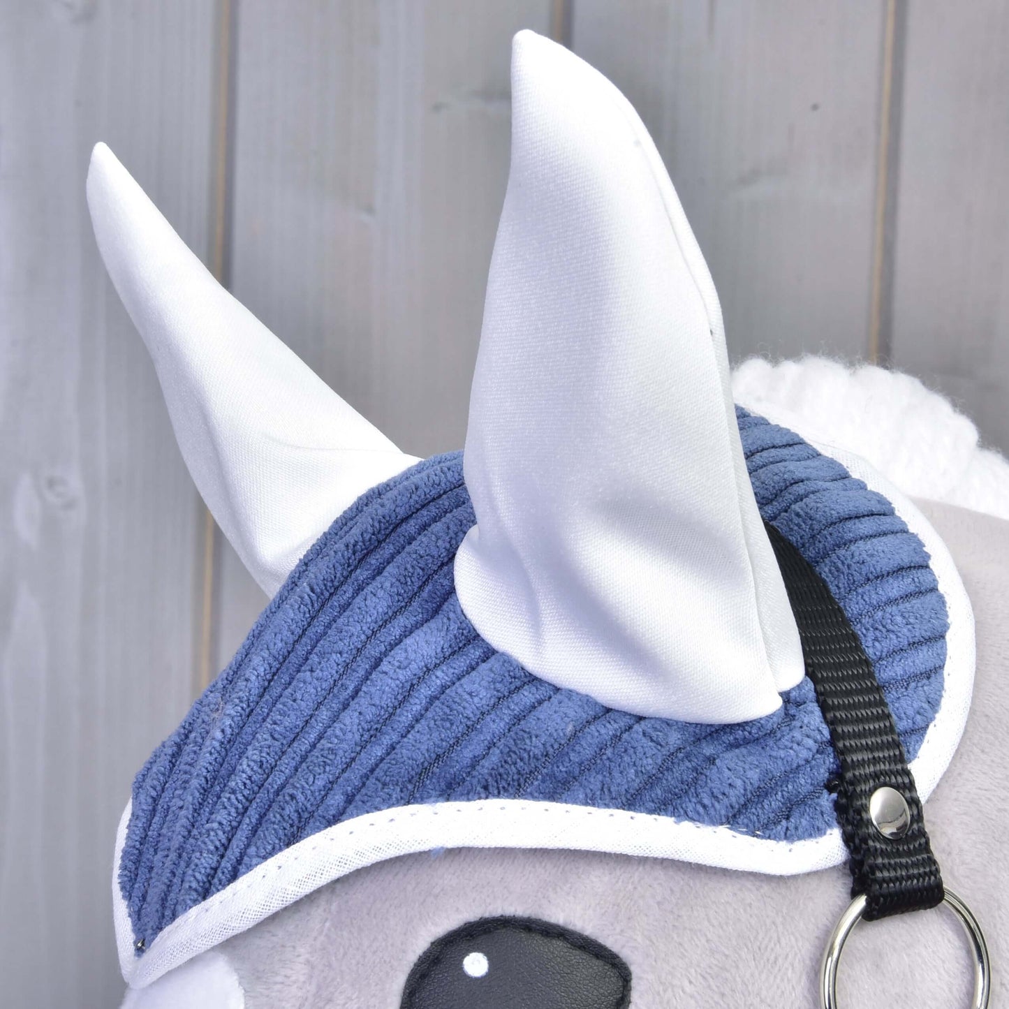 Detail Set Manchester Plum od Hobby Horse LarDen ukazuje bílé látkové uši, modrou manšestrovou čabraku, černý pásek a bílou hřívu na světlém dřevěném pozadí.