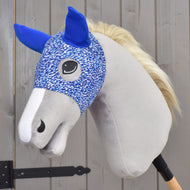 Maska See od Hobby Horse LarDen, plyšový Hobby Horse s modro-bílou pratelnou maskou z PES, modrýma ušima, světle šedým obličejem a bílou hřívou, připevněný na tyči a umístěný před dřevěným plotem.