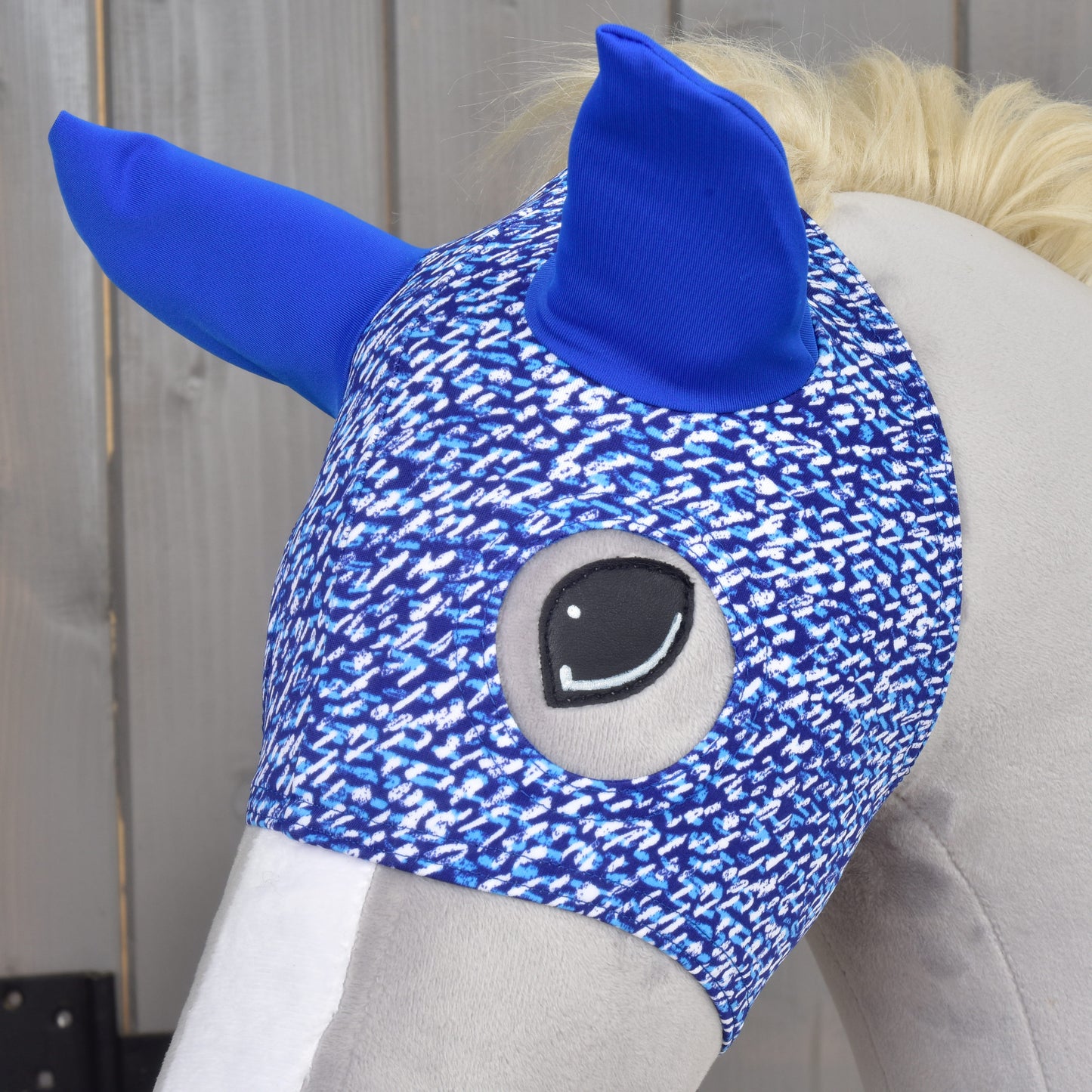 Maska See od Hobby Horse LarDen, detail hlavy plyšového koně s modrýma ušima a modrobílým vzorem na dřevěném pozadí.