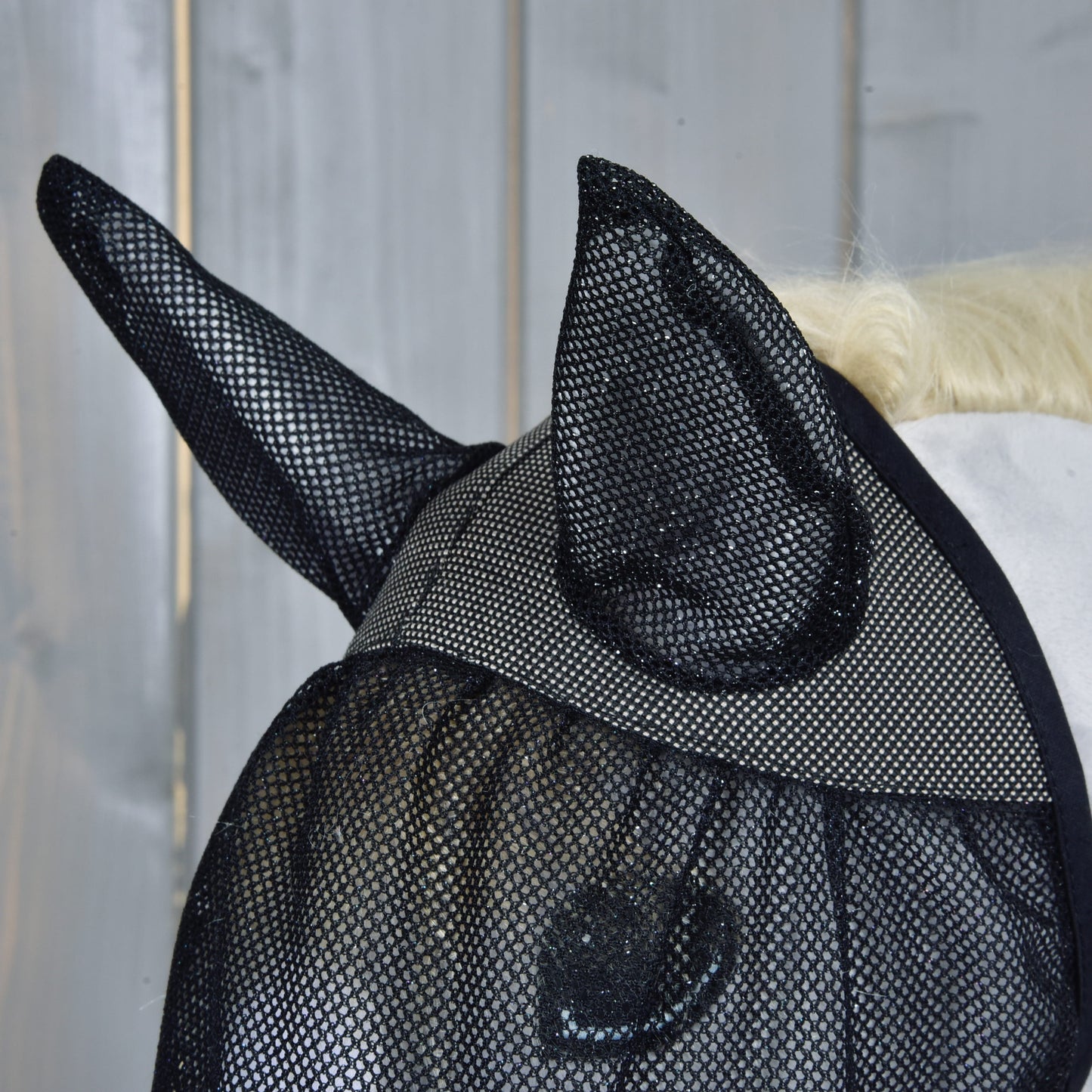 Detail koňské hlavy s maskou proti hmyzu de Luxe Full od Hobby Horse LarDen pro ochranu, s dřevěnou stěnou v pozadí.