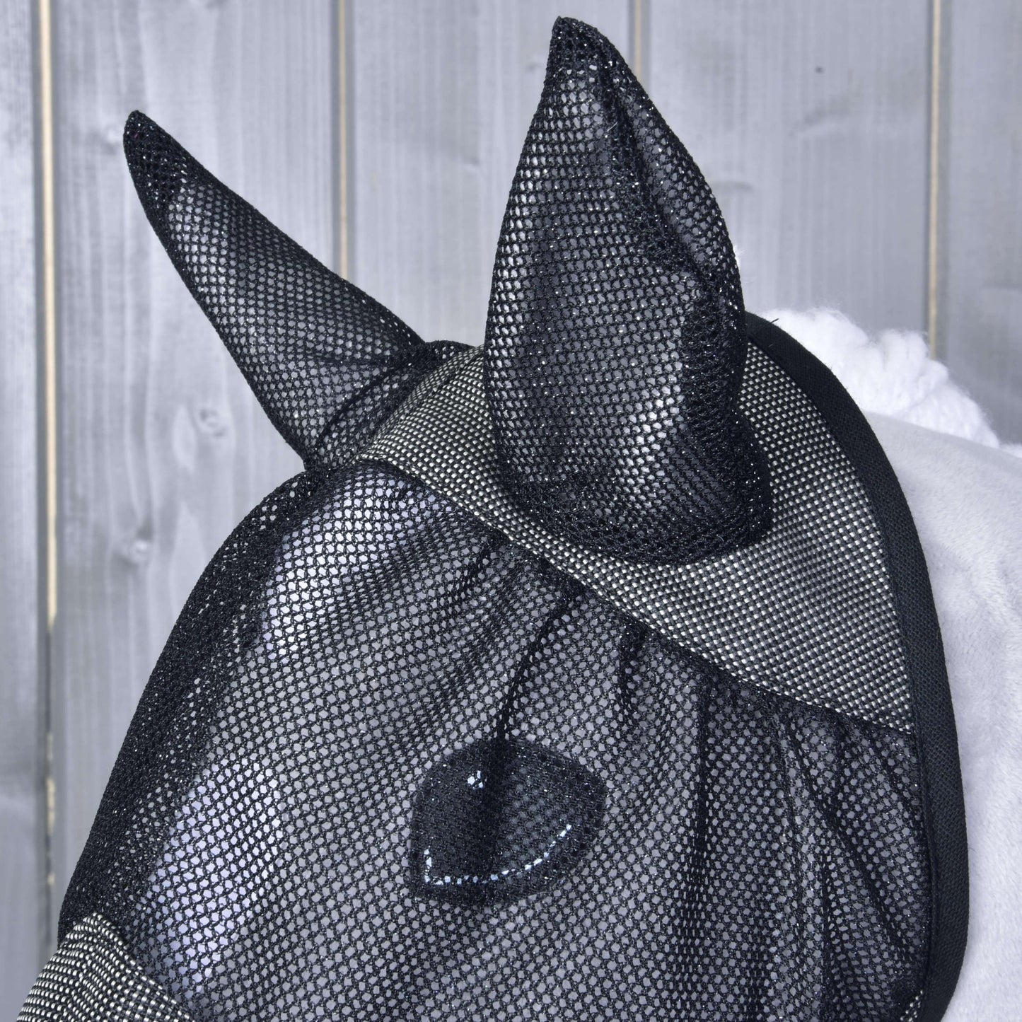 Detail koně v masce proti hmyzu de Luxe Grey od Hobby Horse LarDen se zakrytýma ušima na světle šedém dřevěném pozadí.