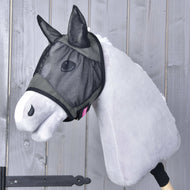 Plyšový Hobby Horse se světle šedou srstí má na sobě Maska proti hmyzu de Luxe Grey od Hobby Horse LarDen pro extra ochranu. V pozadí je stěna ze svislých dřevěných prken.
