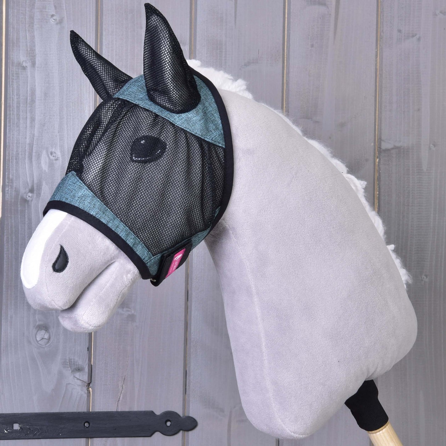 Maska proti hmyzu de Luxe Turquoise od Hobby Horse LarDen je nasazená na šedém plyšovém hobby horse s bílým čenichem, pózujícím před dřevěnými prkny. Omyvatelná maska poskytuje stylovou ochranu pro váš Hobby Horse.