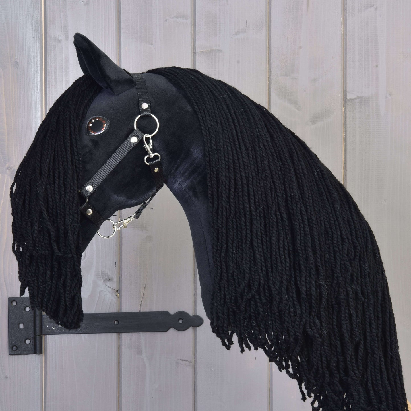 Hobby Horse Maximus s černou ohlávkou od Hobby Horse LarDen, ručně vyráběná hračka černého hřebce s dlouhou přízovou hřívou, lesklou černou uzdečkou a knoflíkovým okem, upevněná na dřevě s černým kovovým držákem.