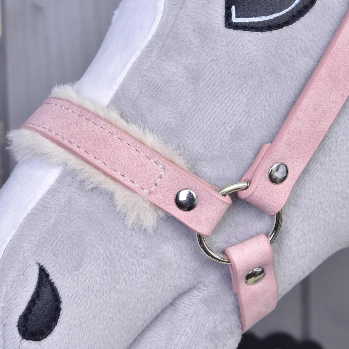 Detail šedého plyšového hračkového koně s Hobby Horse LarDen Ohlávka s beránkem z koženky Mullbery, se světle růžovou koženkou, bílým lemem z umělé kožešiny a vyšívanými černými detaily oka a nozder.