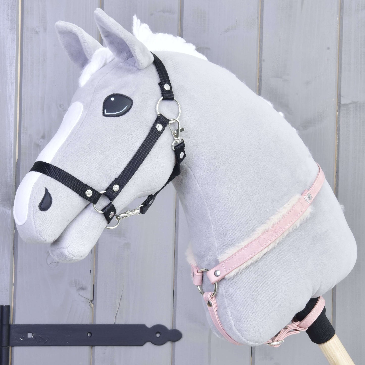 Poprsák s beránkem Mullbery od Hobby Horse LarDen na šedém plyšovém Hobby Horse s bílou hřívou, černou uzdečkou, růžovou ohlávkou a měkkým kožešinovým poprsákem na dřevěné tyči, na světle šedém dřevěném pozadí.