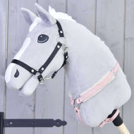 Poprsák s beránkem Mullbery od Hobby Horse LarDen na šedém plyšovém Hobby Horse s bílou hřívou, černou uzdečkou, růžovou ohlávkou a měkkým kožešinovým poprsákem na dřevěné tyči, na světle šedém dřevěném pozadí.