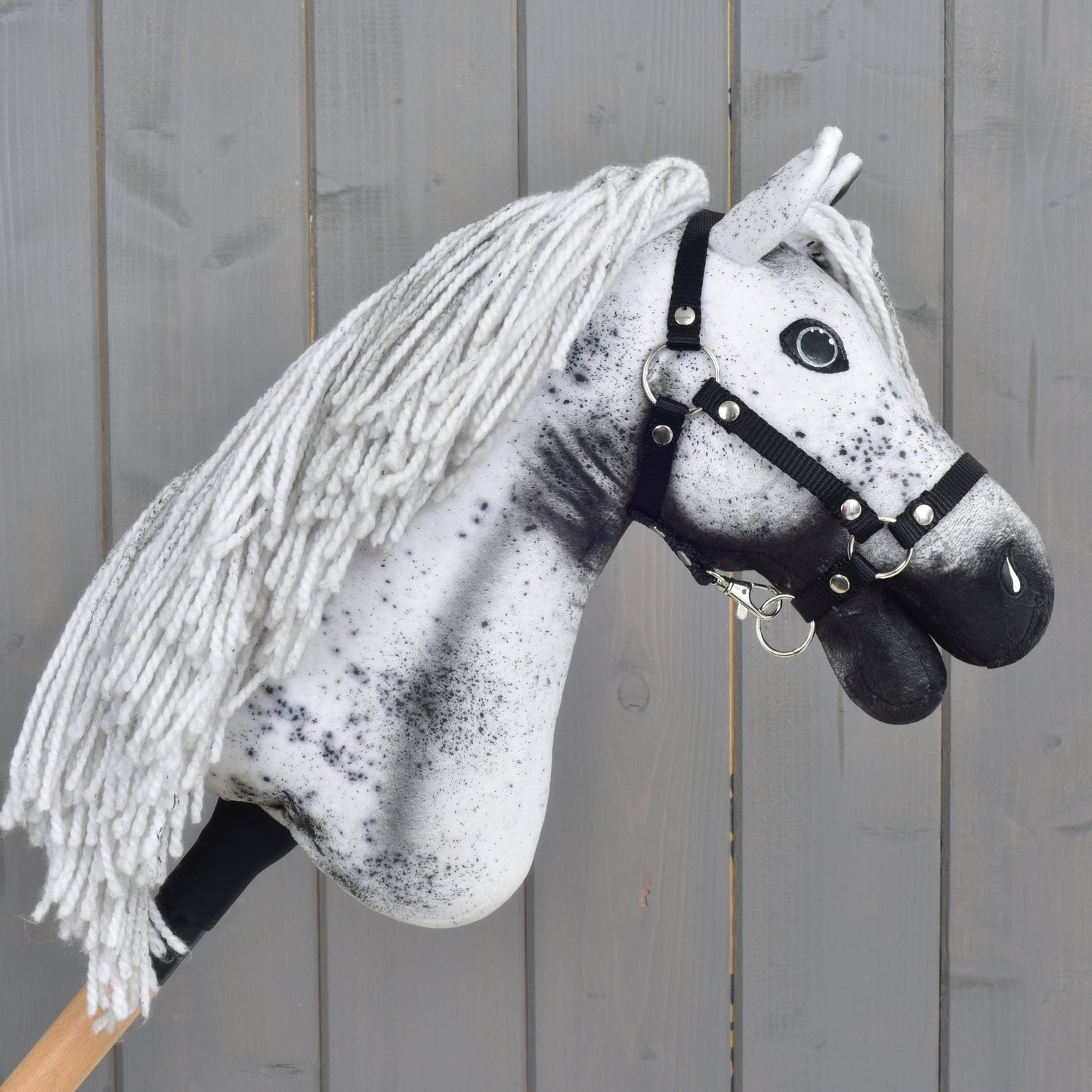 Hobby Horse LarDen "Hobby Horse Naivy with Black Halter" (velikost S): ručně vyrobený Hobby Horse ve vzhledu Appaloosy s bílo-šedou přízovou hřívou, výraznými černými skvrnami a elegantní černou ohlávkou, zasazený do rustikálního dřevěného pozadí. Perfektní pro nápaditá dobrodružství hřebce!