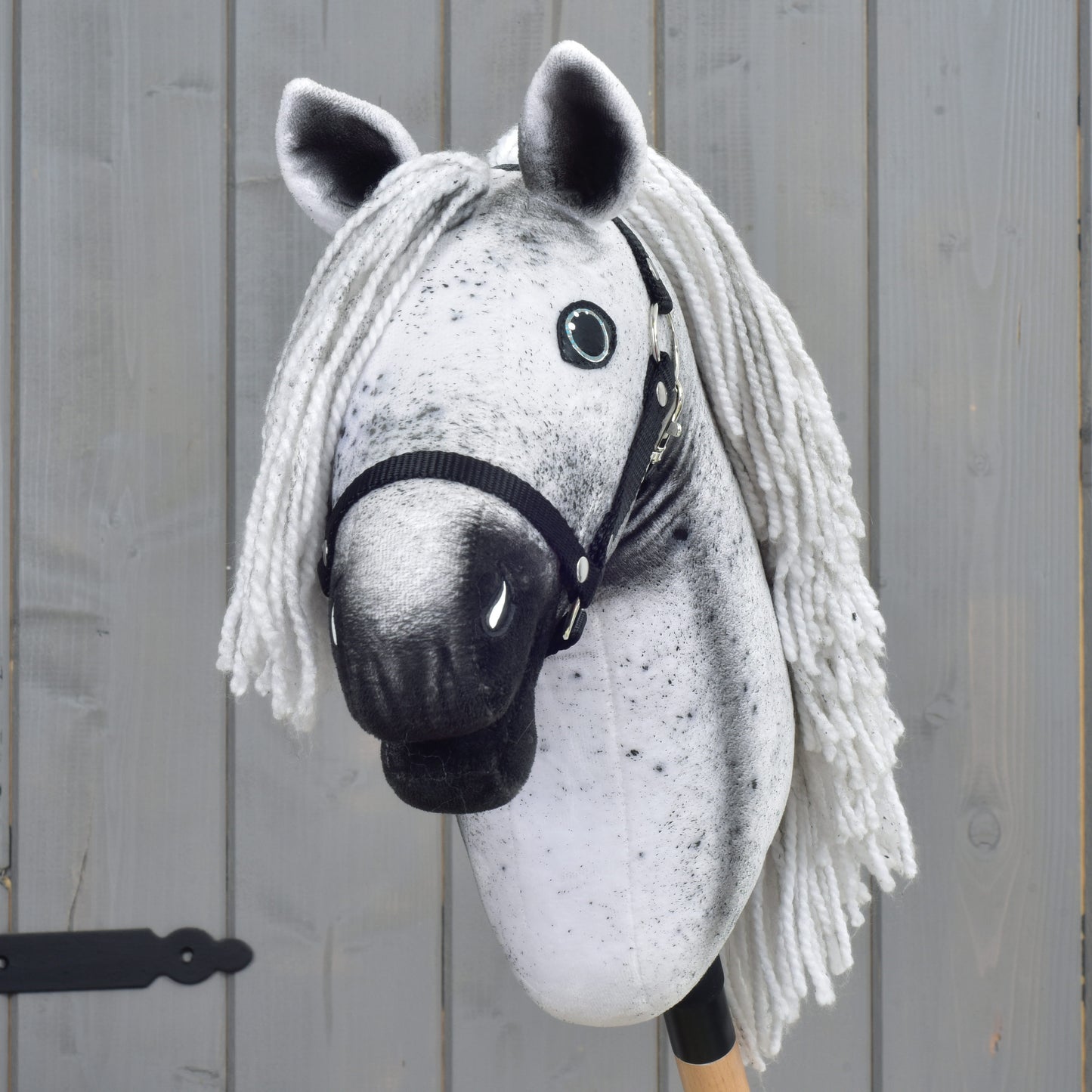 Šedý Hobby Horse LarDen "Naivy" s bílou přízovou hřívou, černou ohlávkou a knoflíkovýma očima (velikost S), umístěný před dřevěným plotem.