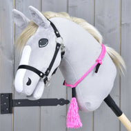 Hobby Horse LarDen „Nákrčník Pink Festive“ na plyšovém šedém Hobby Horse s bílou hřívou, černou uzdečkou, ručně vyrobeným cordeem, růžovým lanovým nákrčníkem a růžovým střapcem, na dřevěném pozadí.