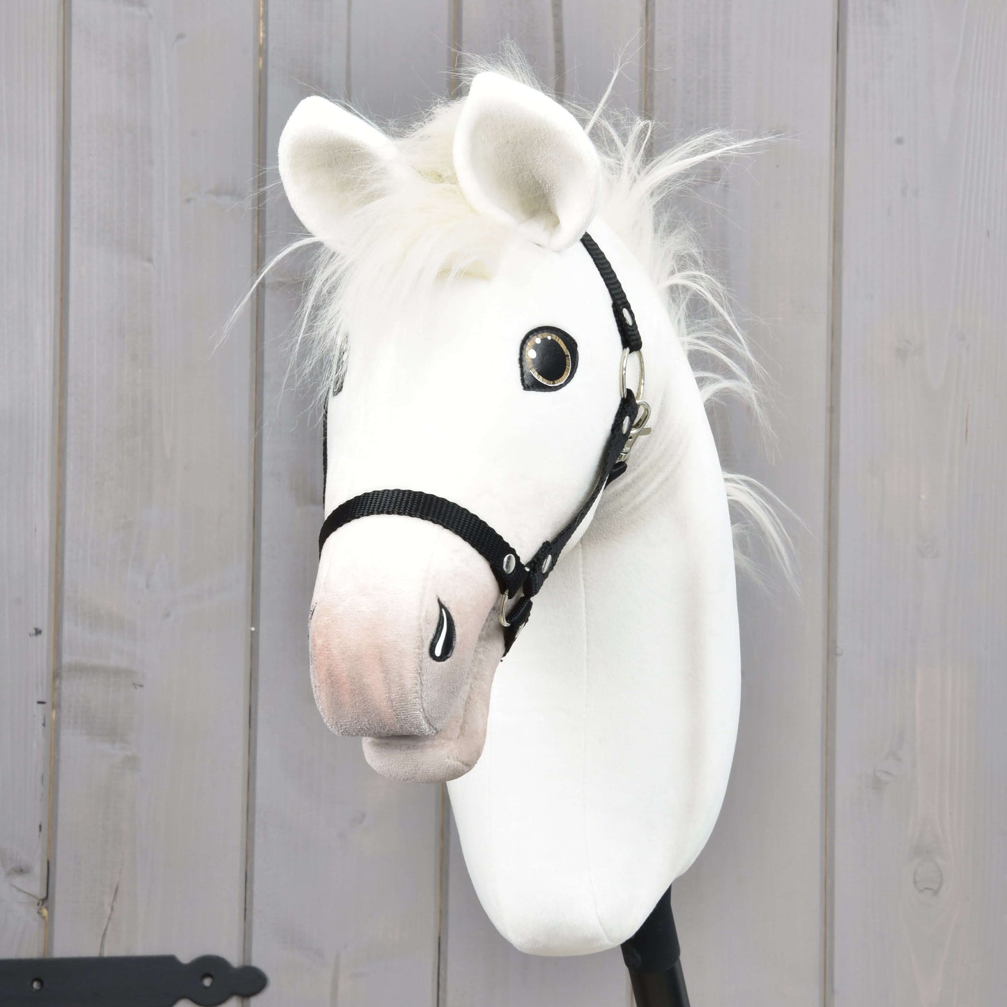 Hobby Horse Nexus s černou ohlávkou od Hobby Horse LarDen, bílý látkový Hobby Horse s měkkou hřívou a lesklýma očima, zobrazený na pozadí světlých dřevěných panelů.
