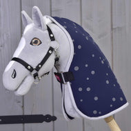 Šedý plyšový Hobby Horse od Hobby Horse LarDen s černou uzdečkou a Dekou stájovou Night Sky, nasazený na dřevěné tyči na pozadí světlé dřevěné stěny.