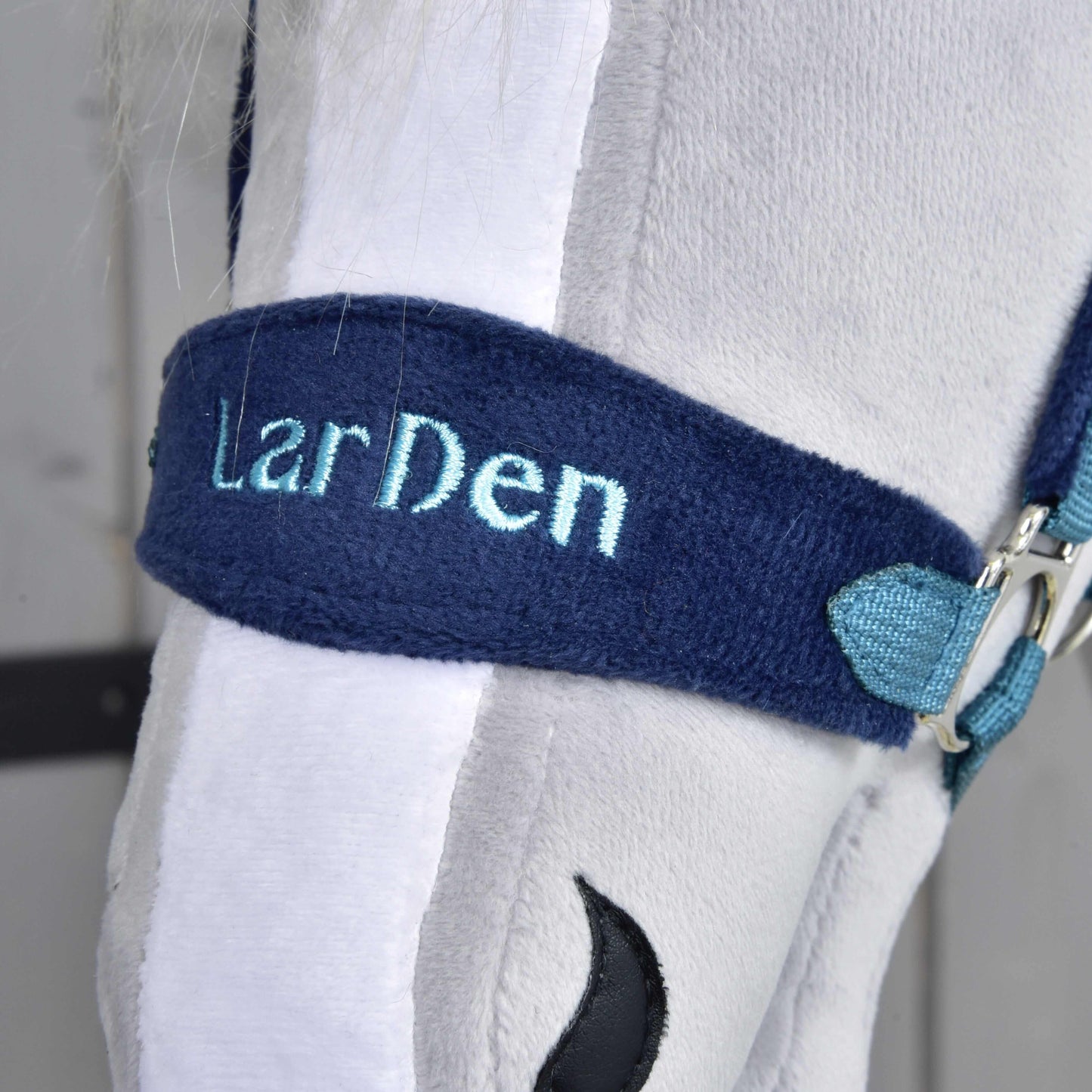 Detail hlavy bílého plyšového koně s ohlávkou s beránkem LarDen Blue od Hobby Horse LarDen, s výšivkou světle modrého textu – stylový doplněk do každé kolekce ohlávek pro hobby horse.