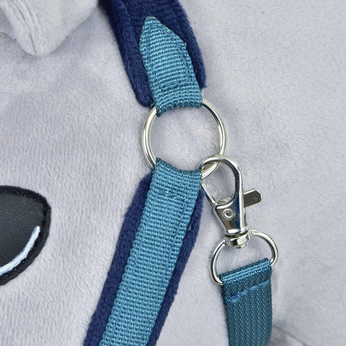Detail kovové karabiny a kroužku spojujících dva modré nylonové popruhy na měkké světle šedé kožešině, s černobílým vyšívaným detailem oka z Hobby Horse LarDen Fur Halter LarDen Blue.