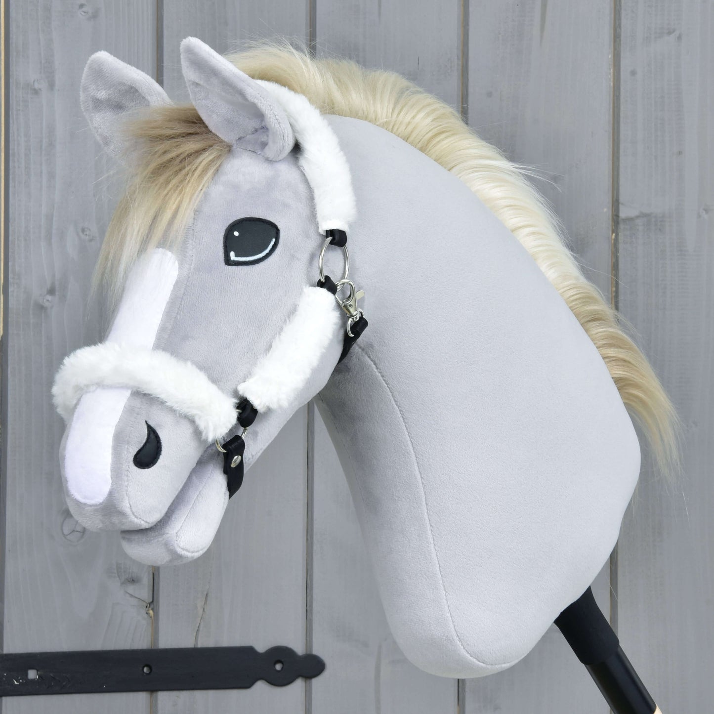 Hobby Horse LarDen Ohlávka s beránkem Teddy Classic na plyšovém Hobby Horse se světle šedou srstí, bílou hřívou, bílými znaky na hlavě a bílou ohlávkou, nasazeném na tyči před dřevěným pozadím.
