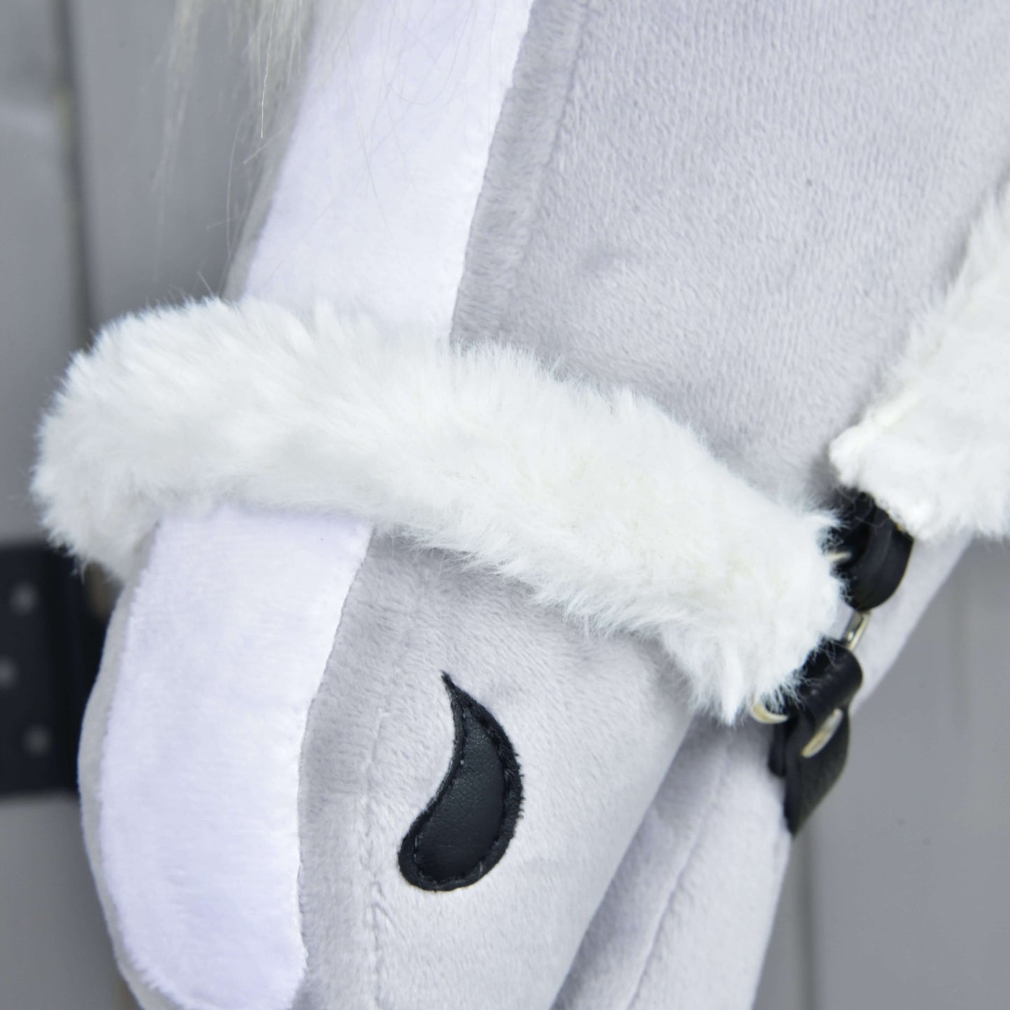 Detail Hobby Horse LarDen Ohlávka s beránkem Teddy Classic na světle šedém plyšovém Hobby Horse s bílou beránkovou ohlávkou a černým vyšitým detailem oka na šedém pozadí.