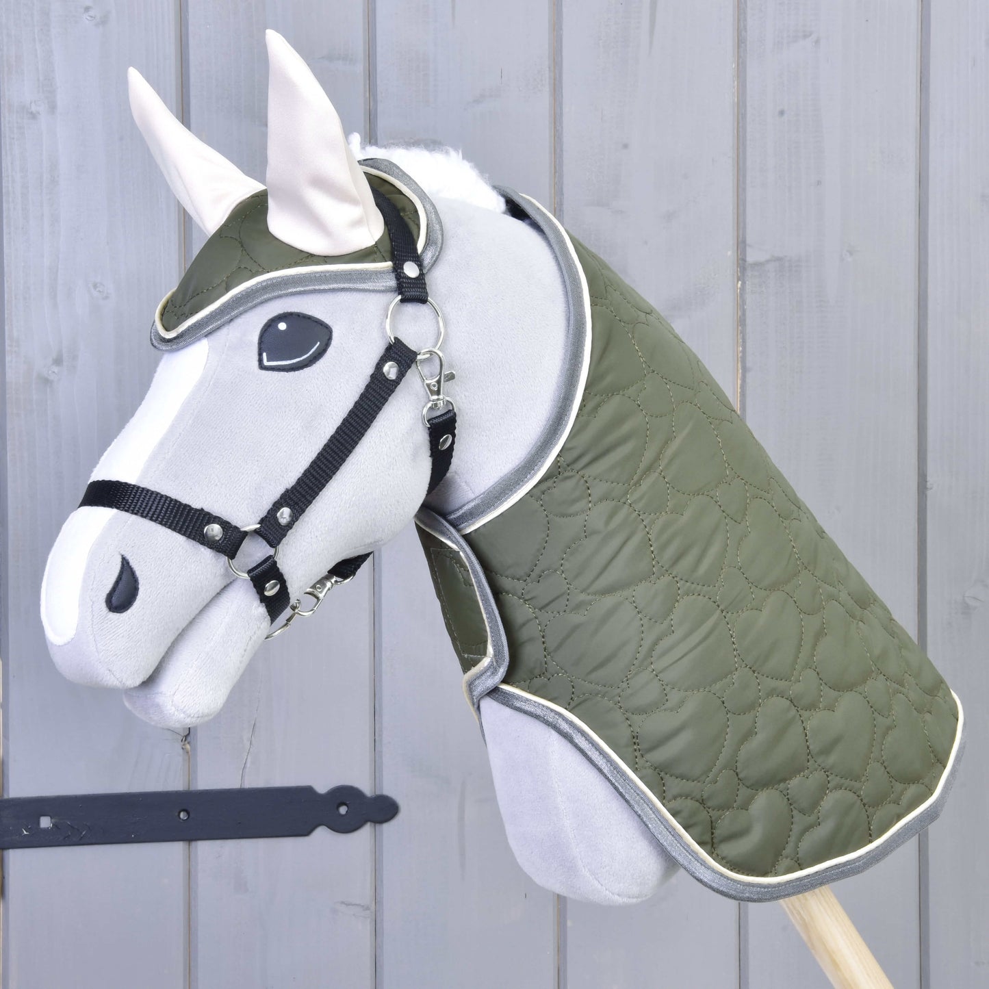 Set Olivetti od Hobby Horse LarDen tvoří šedý Hobby Horse se zelenou prošívanou dekou a uzdečkou, černou ohlávkou, bílými ušima a stylovými doplňky, zobrazený před světle šedou dřevěnou stěnou.