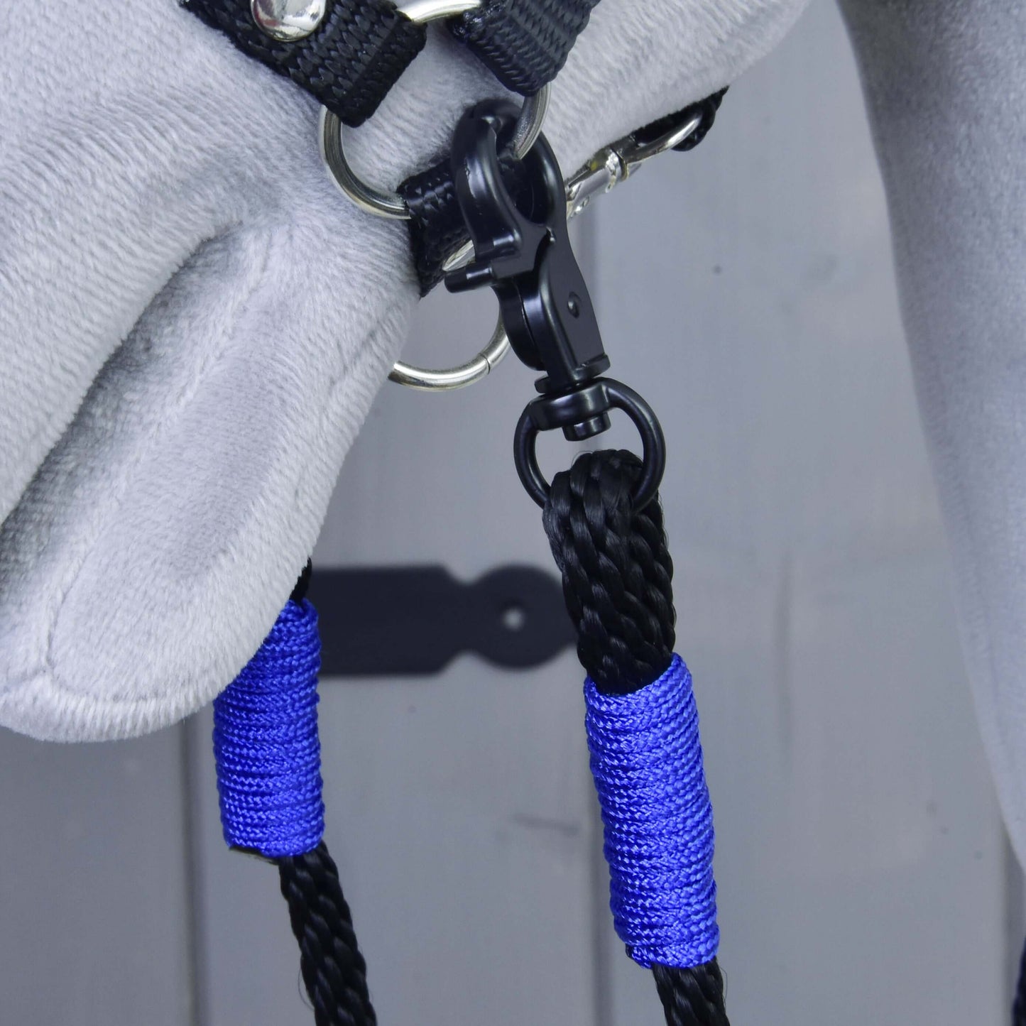 Detail šedé koňské hlavy v černé ohlávce s otěžemi Basic Blue od Hobby Horse LarDen – modro-černé pletené ručně vyráběné polypropylenové otěže připevněné ke kovovému kroužku černou karabinou.