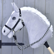 Hobby Horse - otěže černo-bílý proužek od Hobby Horse LarDen na plyšovém šedém Hobby Horse s bílou hřívou a černou uzdou, ručně vyrobené s pruhovanými černo-bílými polypropylenovými otěžemi na dřevěné tyči před světle šedým dřevěným pozadím.