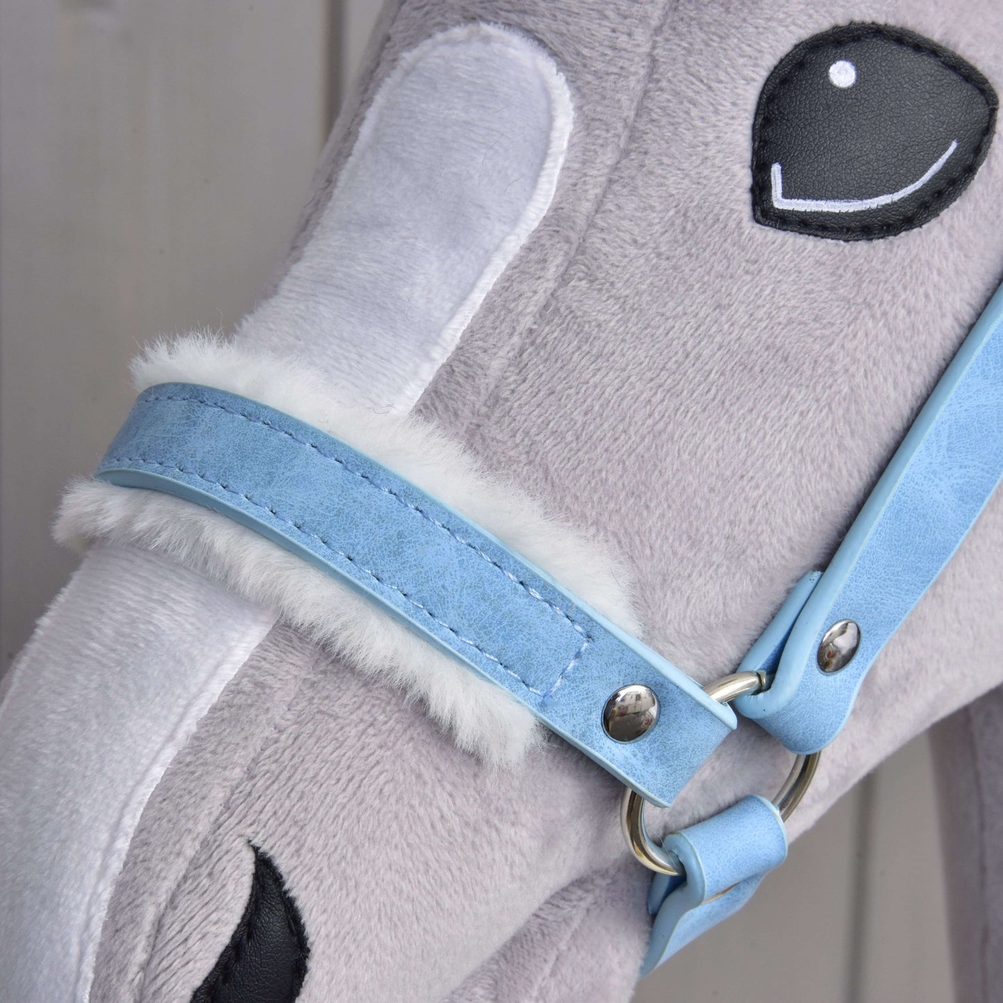 Detail hlavy plyšového hračkového koně s měkkou šedou a bílou srstí, „Ohlávka s beránkem z koženky Pastell Blue“ od Hobby Horse LarDen a vyšívanýma černobílýma očima.