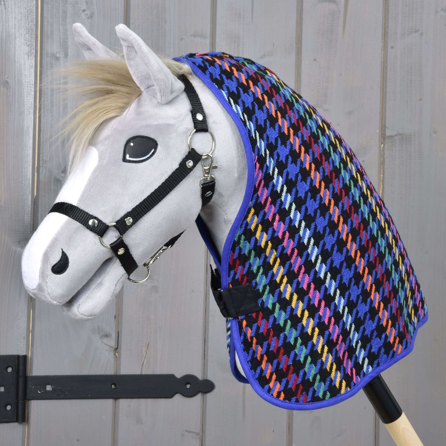 Bílý hračkový Hobby Horse s černou ohlávkou má na sobě barevnou Deka stájová Peru od Hobby Horse LarDen se vzorem kohoutí stopy na pozadí světlého dřeva.