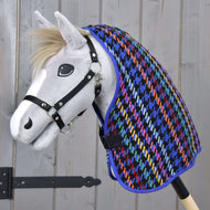Bílý hračkový Hobby Horse s černou ohlávkou má na sobě barevnou Deka stájová Peru od Hobby Horse LarDen se vzorem kohoutí stopy na pozadí světlého dřeva.
