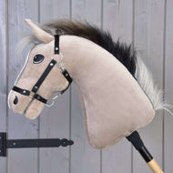 Hobby Horse Piccolino s černou ohlávkou od Hobby Horse LarDen, se světle hnědou hlavou a černou hřívou, na dřevěné tyči, naaranžovaný pro parkurový skok před šedou dřevěnou stěnou.