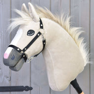 Hobby Horse Pixie s černou ohlávkou od Hobby Horse LarDen, s béžovou srstí, bílou hřívou, černou ohlávkou a výraznýma očima na tyči, stojí před šedým dřevěným pozadím a odkazuje na legendární kovový lesk plemene Akhal-Teke.