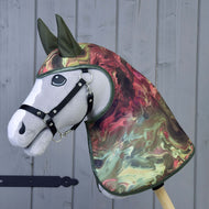 Pláštěnka Galaxy od Hobby Horse LarDen, realistický šedý hobby horse s černou uzdečkou a žíhaným zeleno-červeno-krémovým krytem hlavy a krku ve stylu pláštěnky do každého počasí, zobrazený na dřevěném pozadí.