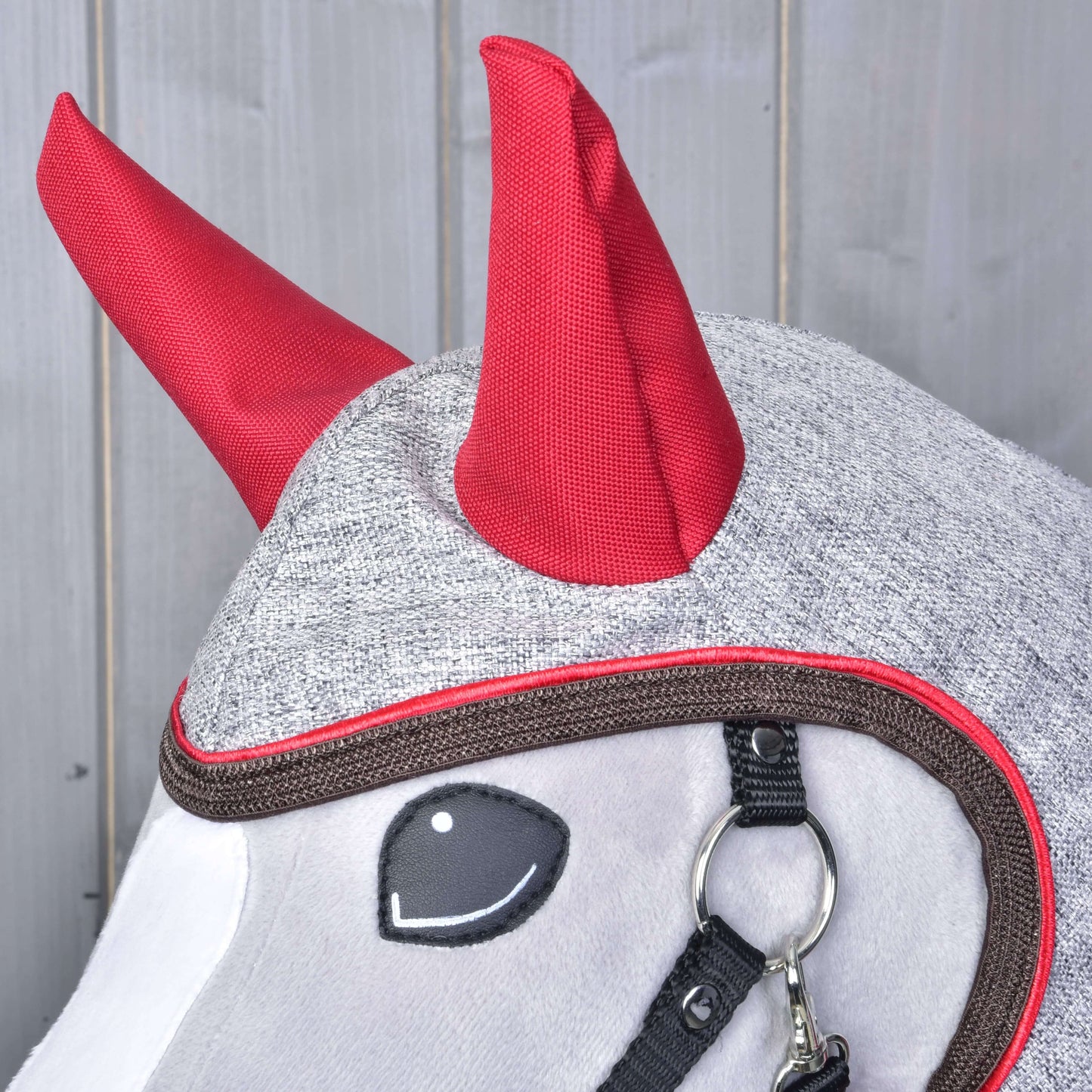 Pláštěnka Leonardo od Hobby Horse LarDen z šedé látky s výraznými červenými detaily připomínajícími rohy a černým postrojem, zobrazená na koni na dřevěném pozadí.