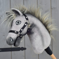 Hobby Horse Prestige s černou ohlávkou, velikost XS od Hobby Horse LarDen s šedým plyšovým provedením, rozcuchanou hřívou a černou ohlávkou, inspirovaný elegancí anglického teplokrevníka. Je nasazený na dřevěné tyči a vystavený na pozadí dřevěného panelu.
