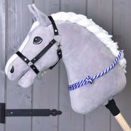 Nákrčník proužek modrý od Hobby Horse LarDen na šedém plyšovém Hobby Horse s bílou hřívou, černou ohlávkou a modře pruhovaným cordeem, na dřevěné tyči před šedou dřevěnou stěnou.