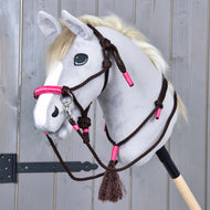 Provazový set Noir Cocoa od Hobby Horse LarDen s plyšovou koňskou hlavou v bílé a šedé barvě, černýma knoflíkovýma očima, krémovou hřívou a hnědo-růžovou ohlávkou s otěžemi, nasazenou na dřevěné tyči, na pozadí panelu.