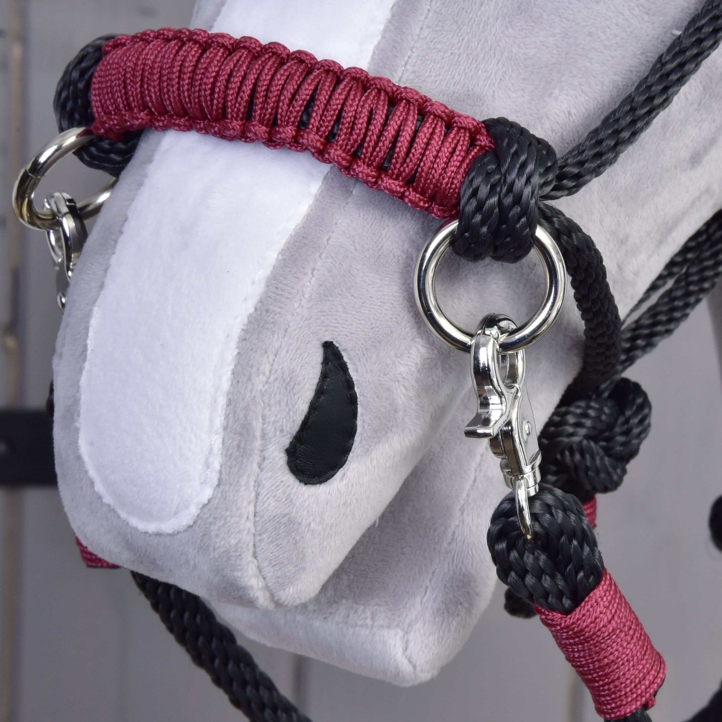 Detail šedo-bílé hlavy Hobby Horse LarDen s nasazeným Provazovým setem Maroon, s černým provazem, kovovými kroužky, klipy a propracovaným prošíváním na látce.