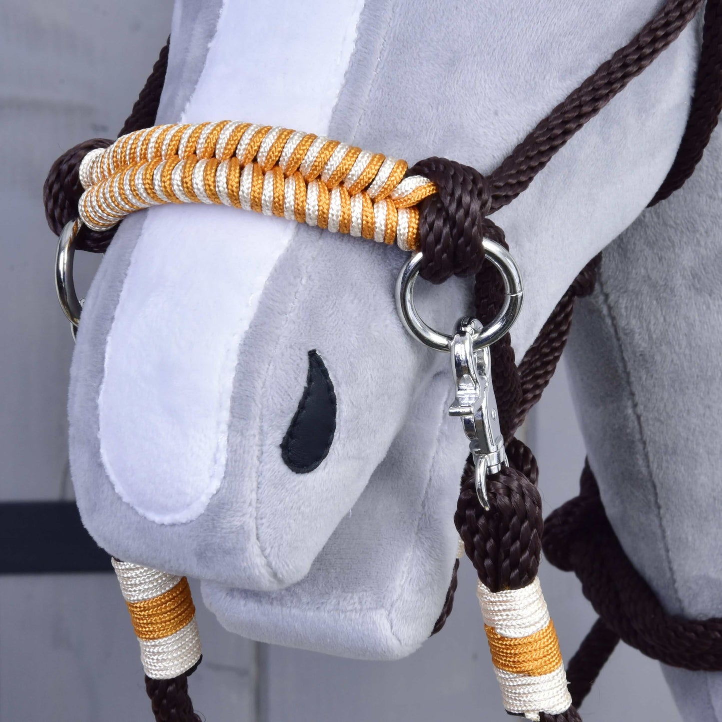 Provazový set Orange od Hobby Horse LarDen, detail hlavy sady s uzdečkou v oranžové barvě, stříbrným kováním a ladícími oranžovými otěžemi. Plyšová hračka má šedý obličej, bílý pruh na nose a černou oválnou nozdru.