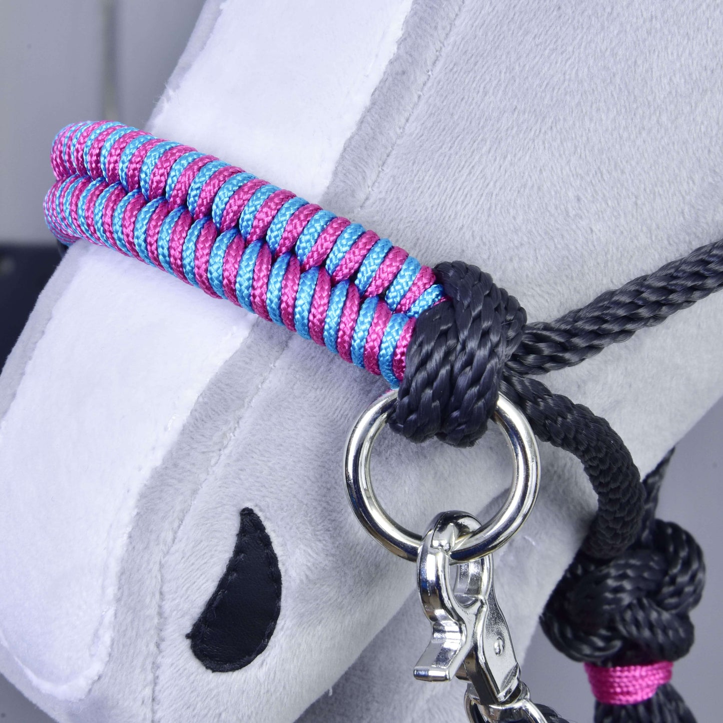 Detailní záběr na hlavu šedého plyšového Hobby Horse s „Provazový set Princess“ od Hobby Horse LarDen – růžovo-modrá pletená ohlávka s černými provazovými detaily, kovovým kroužkem a stříbrnou karabinou. Černé prošití tvoří nozdry a oči pro nápaditou hru.
