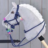 Provazový set Rosemary od Hobby Horse LarDen na šedém plyšovém Hobby Horse s bílou hřívou, tmavě modrými otěžemi a ohlávkou s neonovými korálky, nasazeném na dřevěné tyči před šedým dřevěným pozadím.