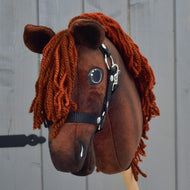 Hobby Horse Rebel s černou ohlávkou - velikost XS od Hobby Horse LarDen, hnědý látkový model navržený tak, aby připomínal hannoverského hřebce, s oranžovou přízovou hřívou, vystavený před šedou dřevěnou stěnou.
