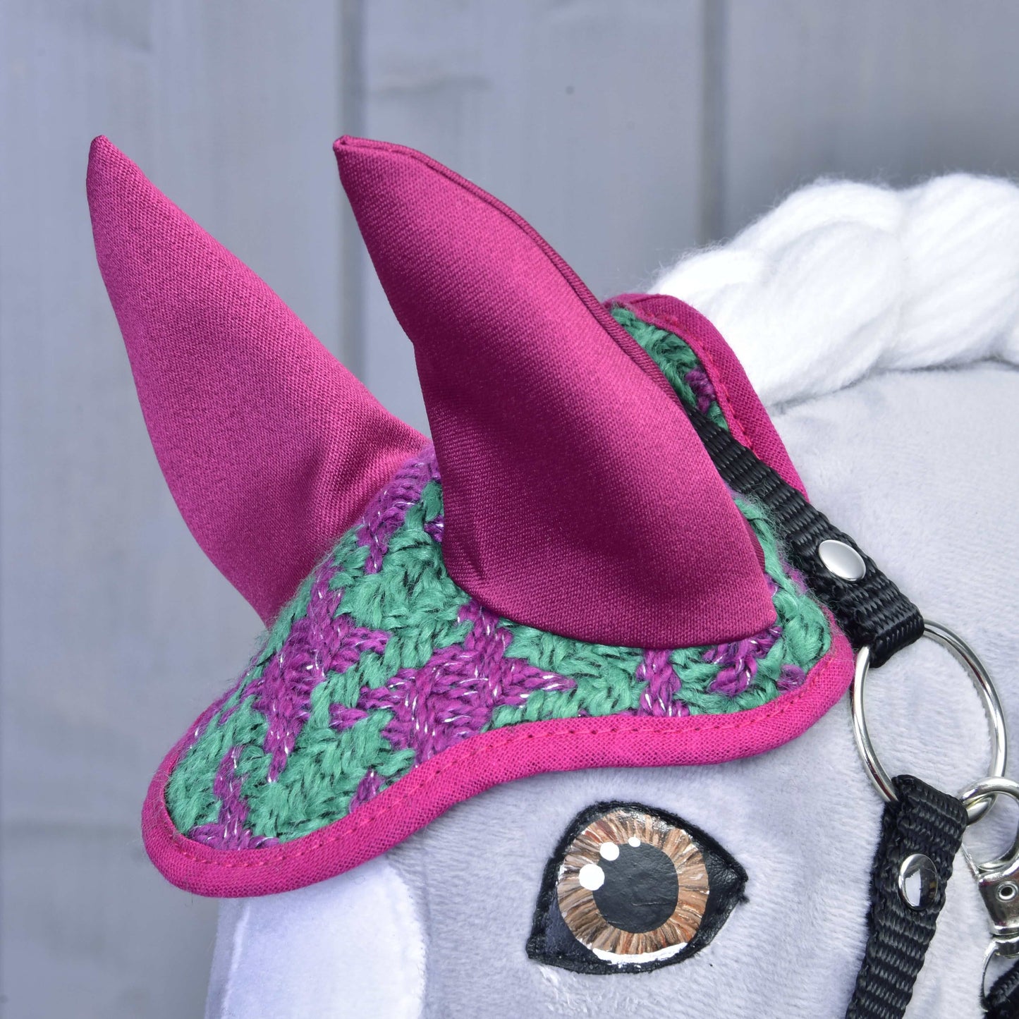Detail Set Coco od Hobby Horse LarDen: šedá hlava s háčkovanou zeleno-fialovou čabrakou na uši, velkými růžovými látkovými ušima, bílou hřívou a černou uzdečkou s lesklým kovovým kroužkem.