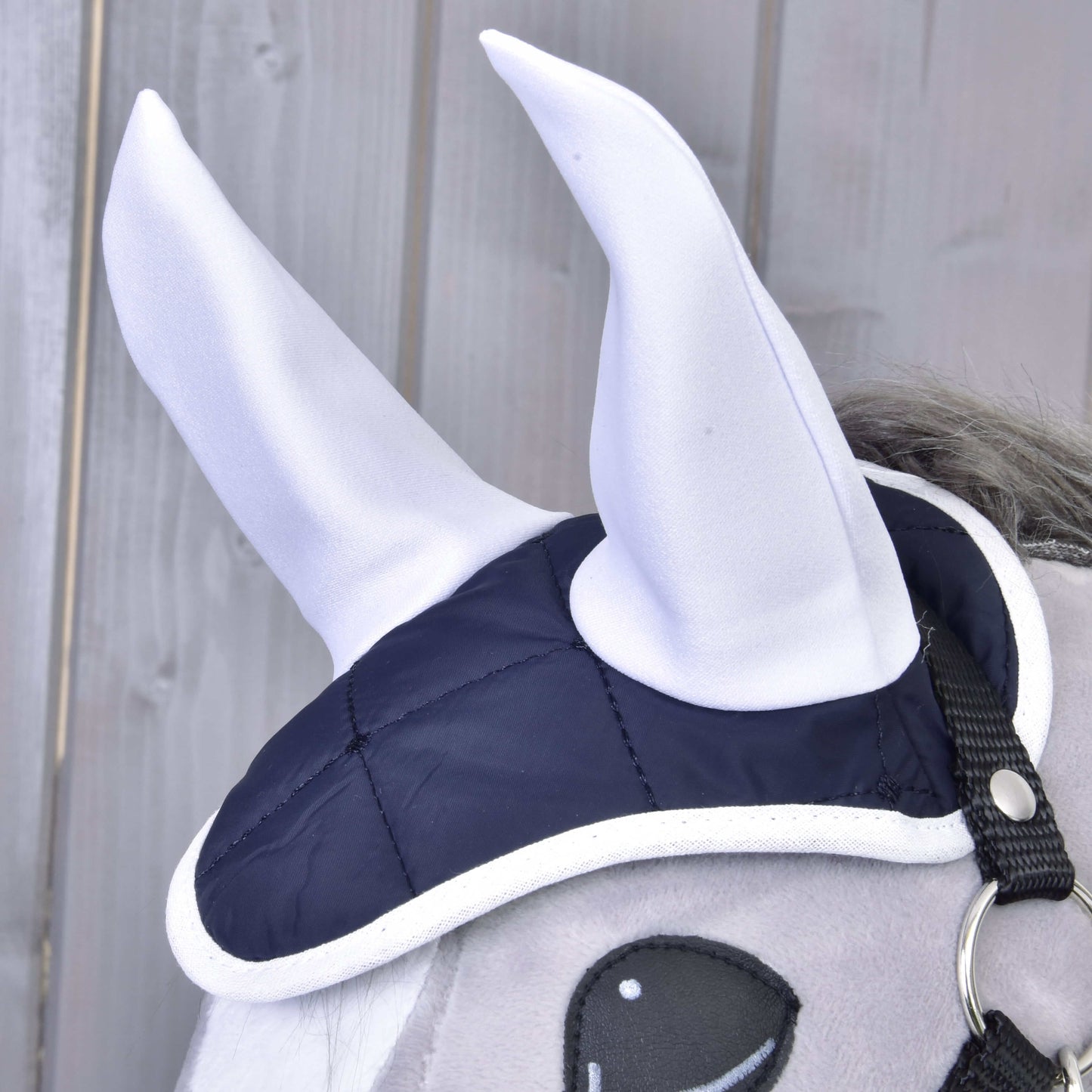 Set Monte od Hobby Horse LarDen: šedá plyšová koňská hlava s tmavě modro-bílou sadou čabraky na uši se dvěma velkými bílými špičatými látkovými rohy, zobrazená před dřevěným obložením pro výrazný vzhled.