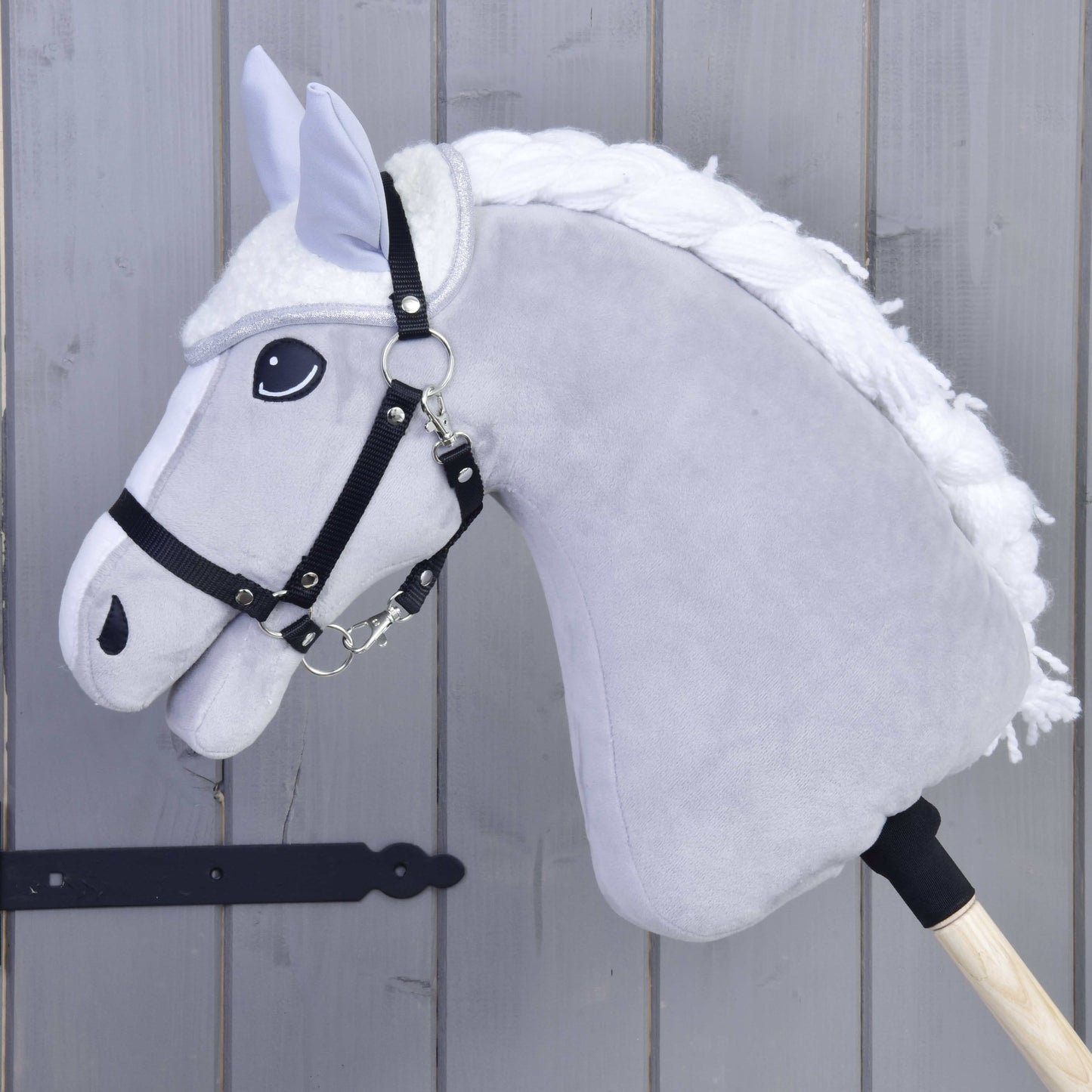 Detail Hobby Horse LarDen Set Snowflake se šedým tělem, bílou hřívou, černou uzdečkou a otěžemi a čabrakou na dřevěné tyči na pozadí šedého dřeva.