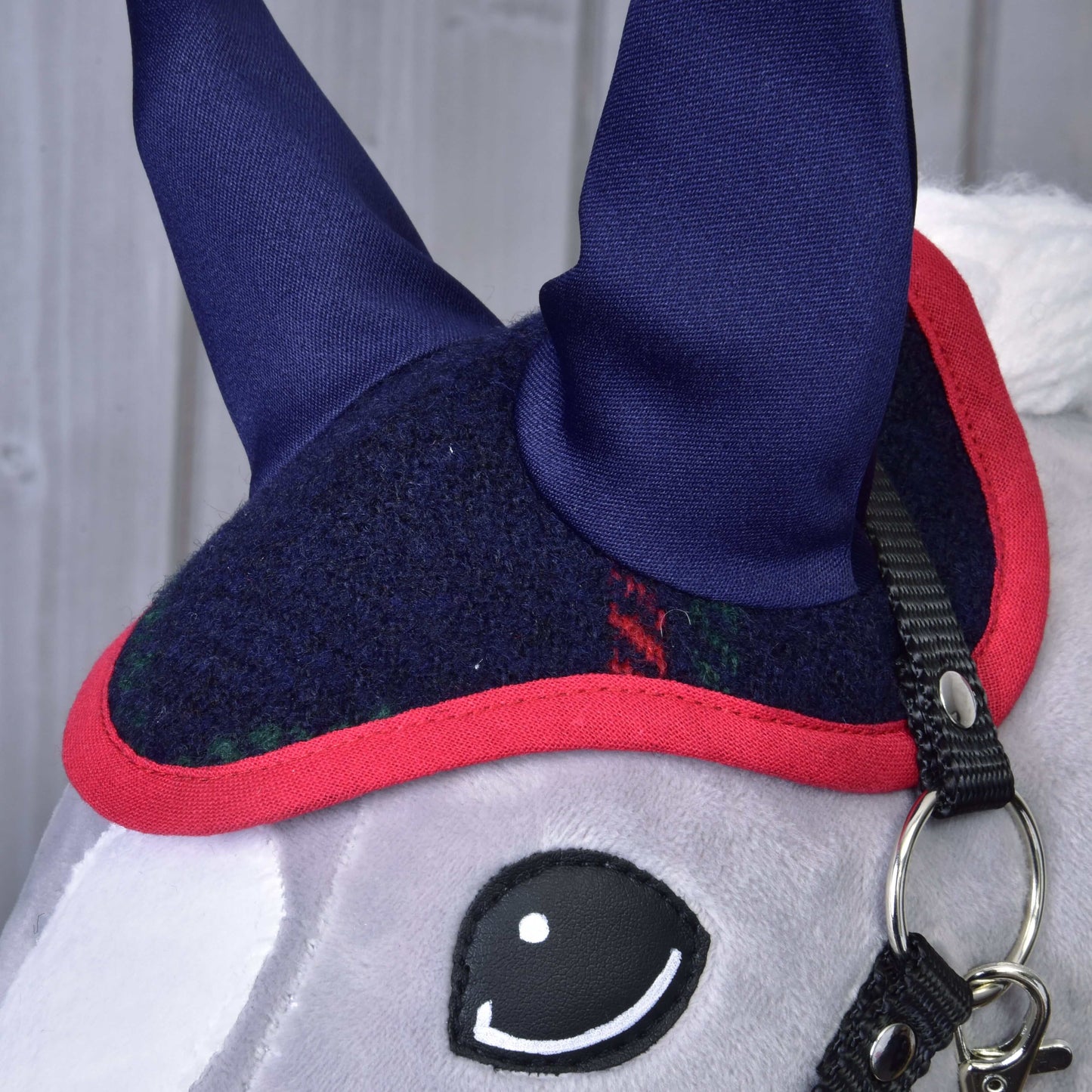Detail sady Set Tartan od Hobby Horse LarDen zobrazuje plyšovou koňskou hlavu s tmavě modrou a červenou čabrakou, špičatýma modrýma ušima, černým páskem se stříbrným kroužkem a světle šedým obličejem s velkým černobílým okem v kresleném stylu.