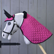 Plyšový Hobby Horse od Hobby Horse LarDen stojící na dřevěné tyči s bílým obličejem, černou uzdečkou a dekou a čabrakou Set Thermo Pink před šedou stěnou, jako půvabná jezdecká dekorace.