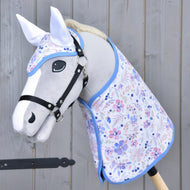 Hobby Horse LarDen Set Vanessa NEW s šedým Hobby Horse, černou uzdečkou, květinovou sadou dečky s modrým lemem a ladící čabrakou, vše zobrazené na dřevěném pozadí.