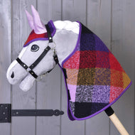 Set podzimní Karo 2 od Hobby Horse LarDen, plyšový hobby horse se šedým obličejem, s černou uzdečkou a barevným patchworkovým kostkovaným krytem krku, upevněný na dřevěné tyči, zobrazený před dřevěnou stěnou.