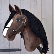 Hobby Horse Sisi s černou ohlávkou od Hobby Horse LarDen, s tmavě hnědou srstí, bílým pruhem na hlavě, černou přízovou hřívou a vzhledem mladého hanoverského sportovního koně, na pozadí dřevěných panelů.