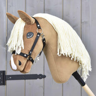 Hobby Horse Smart s černou ohlávkou od Hobby Horse LarDen s plyšovým světle hnědým obličejem, bílou přízovou hřívou a černou ohlávkou na dřevěné tyči, vystavený před šedou dřevěnou stěnou.