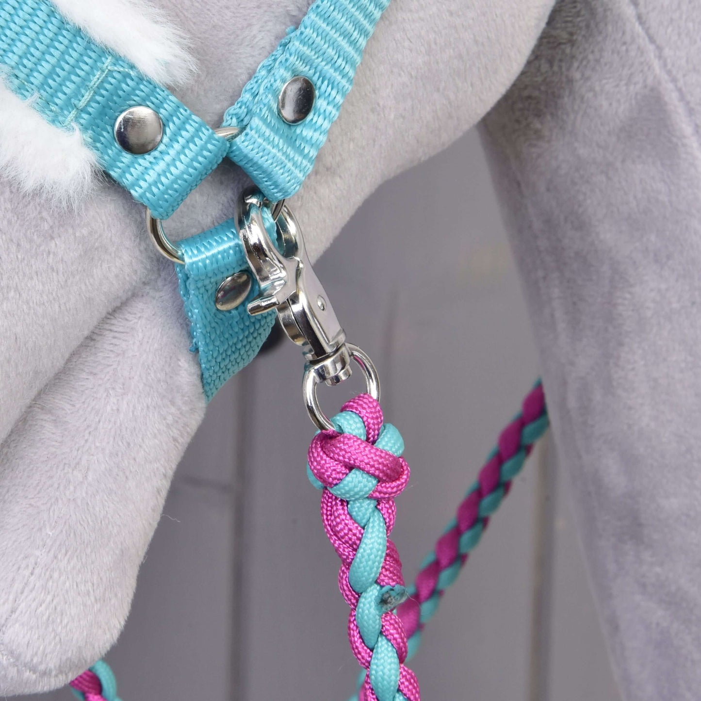 Detailní záběr na Set Perfect Combination Turquoise od Hobby Horse LarDen s pleteným růžovo-modrým vodítkem připnutým k tyrkysové ohlávce s kožešinovým polstrováním na světle šedém plyšovém koni – ideální pro fanoušky doplňků pro hobby horse.