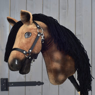 Hobby Horse Stormy s černou ohlávkou od Hobby Horse LarDen, hnědý plyšový model hanoverského koně s černou přízovou hřívou, černou ohlávkou a bílými znaky, nasazený na tyči na pozadí šedého dřeva.